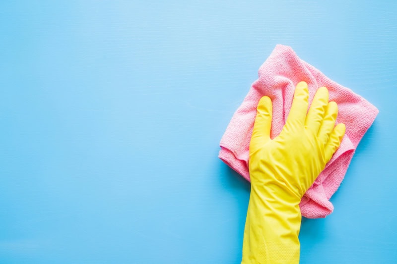 Does An AC Kill Mold? A hand in a yellow rubber glove, wiping a blue wall or table with a pink cloth